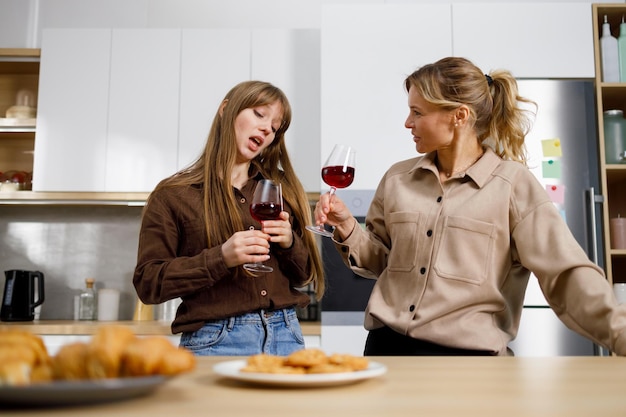 Due donne di età diverse con bicchieri di vino in cucina che parlano