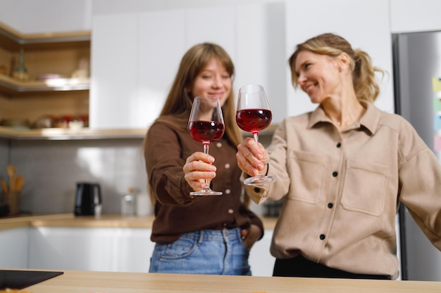 Due donne di età diverse in cucina scandiscono bicchieri di vino rosso.