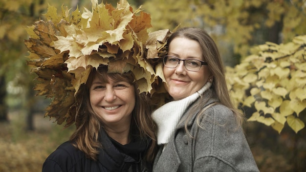 Due donne di mezza età, amiche, camminano nel parco autunnale e ridono. Tonalità marrone d'atmosfera, effetto cinema. Messa a fuoco selettiva. Il concetto di relazione tra donne