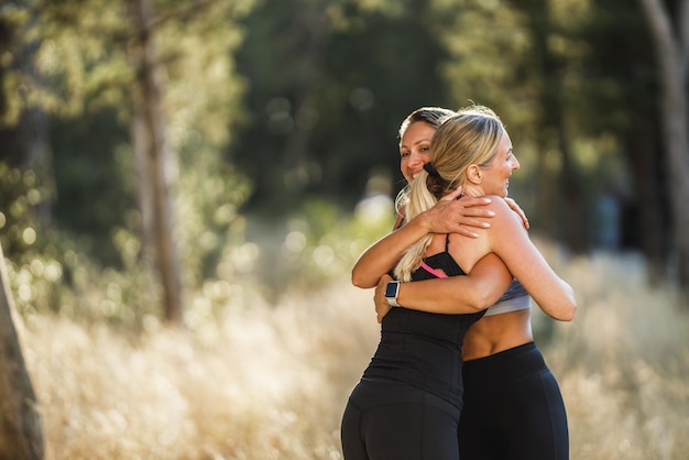 Due donne di mezza età in forma salutano in abbraccio prima dell'allenamento nella pineta vicino alla riva del mare durante il giorno d'estate.