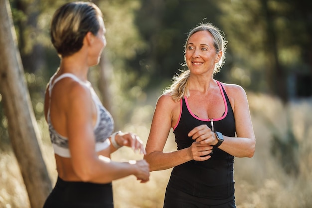 Due donne di mezza età in forma stanno parlando durante la pausa dell'allenamento di corsa nella pineta in una giornata estiva.