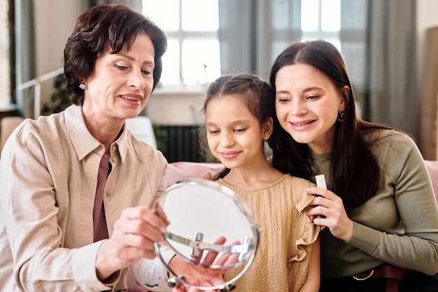 Due donne e una bambina carina che si guardano allo specchio mentre applicano il trucco