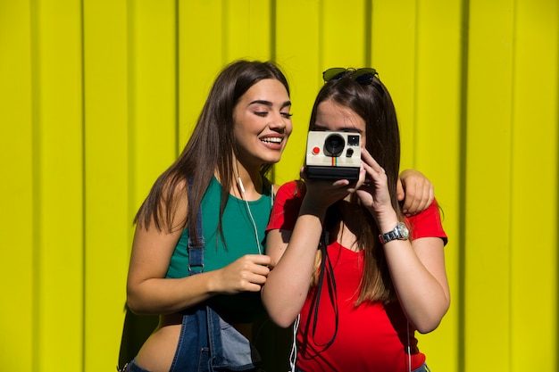 Due donne felici abbastanza giovani che prendono la foto con la retro macchina fotografica e si divertono