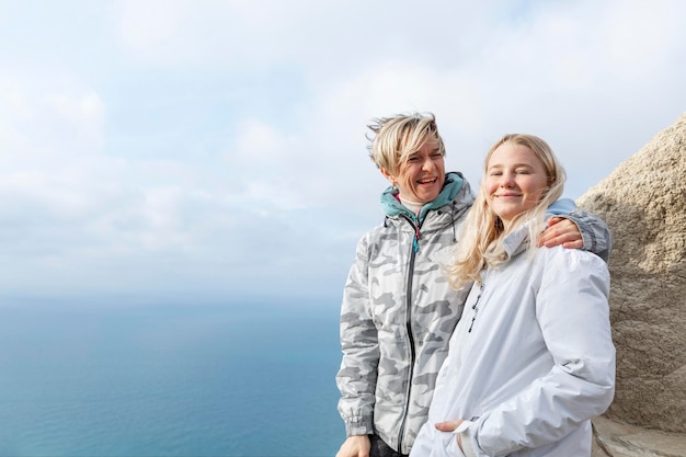 Due donne felici in cima a una montagna sopra il mare in una giornata di sole bionde in giacche sportive abbracciano e sorridono stile di vita attivo viaggi e trekking