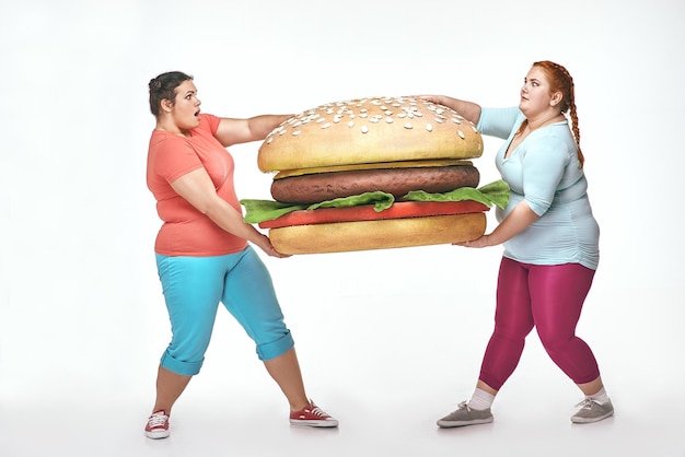 Due donne grassocce tengono in mano un enorme panino
