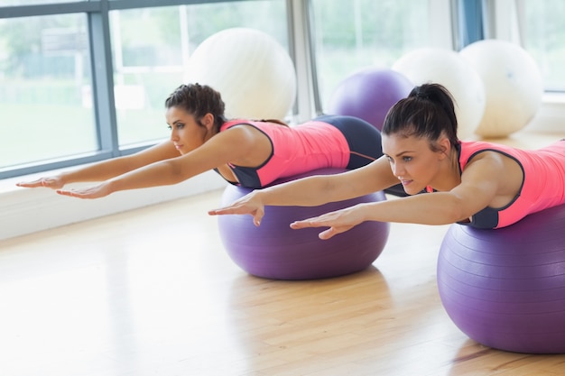 Due donne in forma allungando le mani sulle palle di fitness in palestra