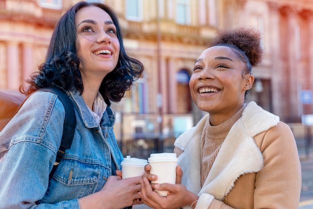 Due donne in giacca di jeans parlano bevendo caffè e aspettano il tram alla fermata Foto di stile di vita