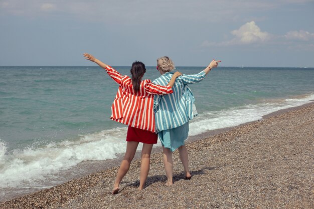 Due donne in giacca e cravatta a righe sono in piedi sulla spiaggia