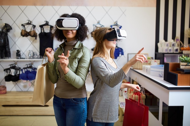 Due donne in moderne cuffie per realtà virtuale che hanno esperienza nello shopping in un negozio di lingerie