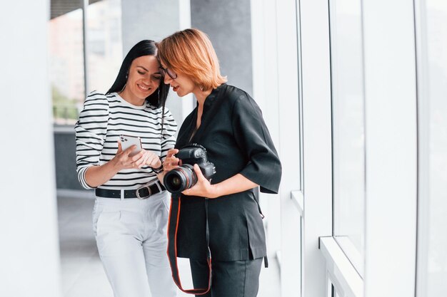 Due donne in piedi al chiuso con fotocamera e telefono in mano