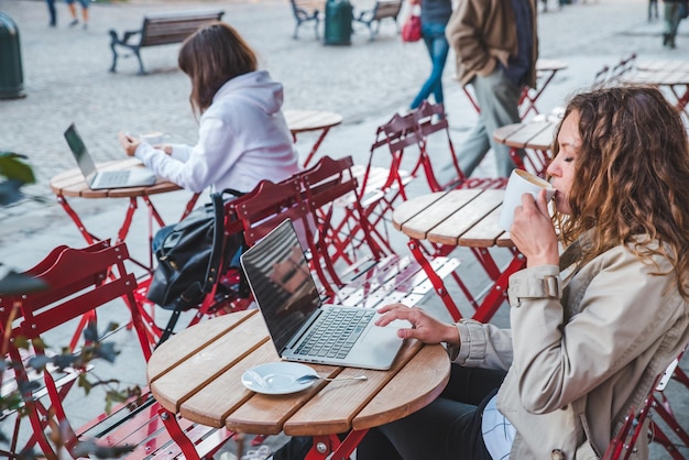 Due donne in un caffè seduto a un tavolo diverso che beve latte lavorando sul computer portatile