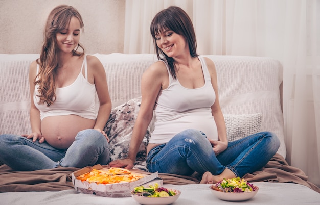 due donne incinte che mangiano pizza e insalata a casa