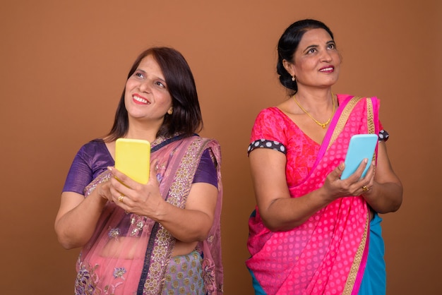 due donne indiane mature che indossano abiti tradizionali indiani Sari insieme allo smartphone