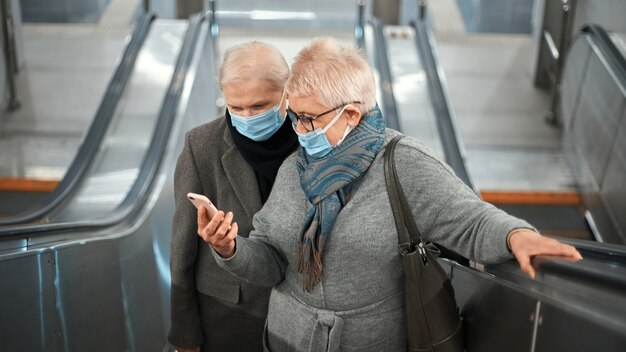 Due donne mature con uno smartphone in piedi su una scala mobile della metropolitana