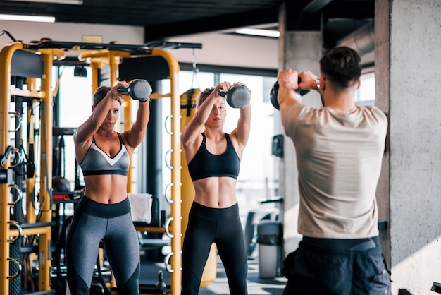 Due donne muscolose che lavorano con trainer in palestra.