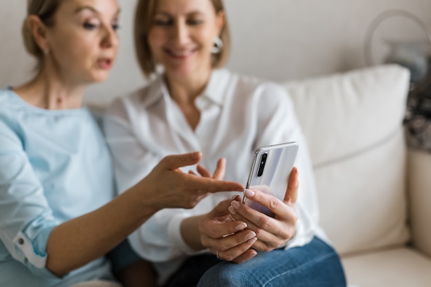 Due donne sono sedute sul divano e guardano il telefono mentre parlano