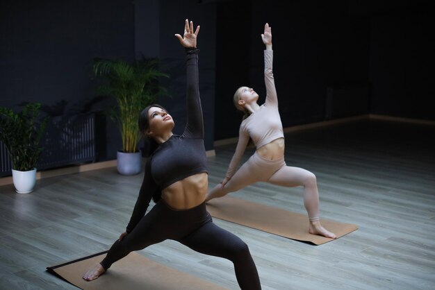 Due donne sportive che praticano facendo yoga pongono il guerriero nello studio di stretching