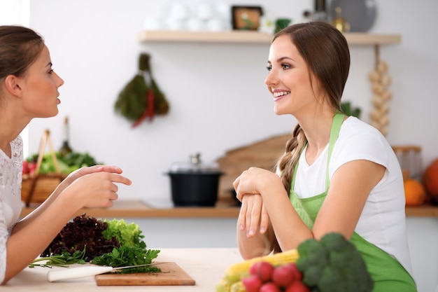 Due donne stanno cucinando in una cucina Amici che si divertono a parlare mentre preparano e assaggiano l'insalata Concetto di Friends Chef Cook