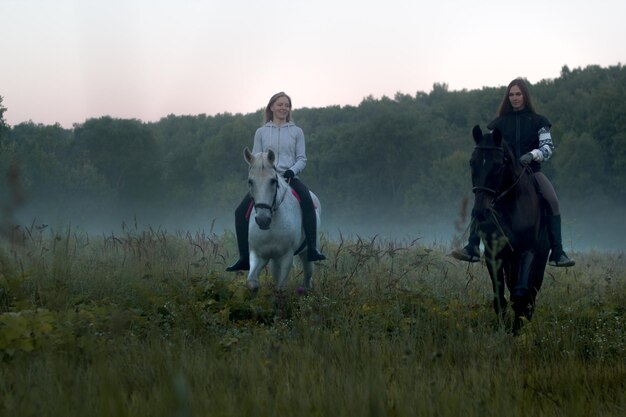 Due donne su un campo nebbioso a cavallo verso la telecamera