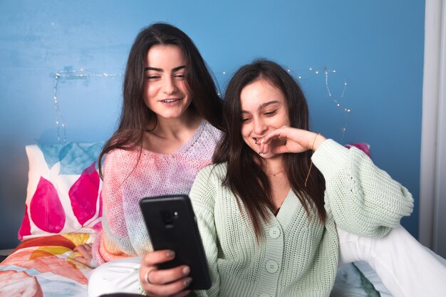 Due donne su un letto che usano uno smartphone