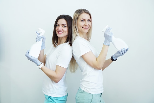 Due donne tengono flacone spray con antisettico o detergente come pistole Salute o concetto di pulizia Covid su sfondo bianco