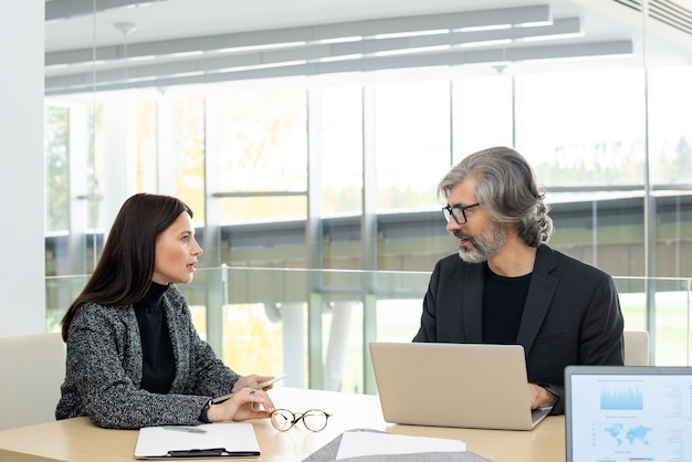 Due economisti fiduciosi che si guardano l'un l'altro durante la discussione di nuove idee per la presentazione o dati finanziari durante una riunione di lavoro in ufficio