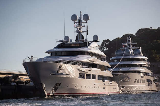 Due enormi yacht sono nel porto di monaco al tramonto il riflesso del sole è su tavole lucide di barche a motore t...