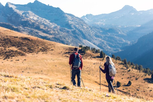 Due escursionisti di viaggio con lo zaino che camminano guardando il paesaggio in montagna. Vista posteriore.