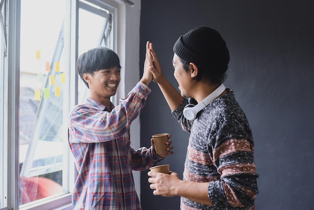 Due felici professionisti amichevoli, in piedi in ufficio che celebrano il successo, buon risultato di cooperazione