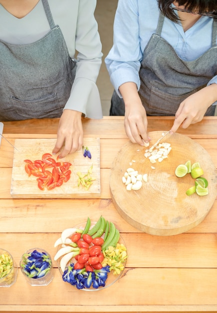 Due femmine asiatiche tagliate l'aglio e il pomodoro con un coltello sul tagliere di legno con mezzo lime fiore di primula farfalla piselli cipollotto piselli e uova in quella zona poi preparando per il pranzo.