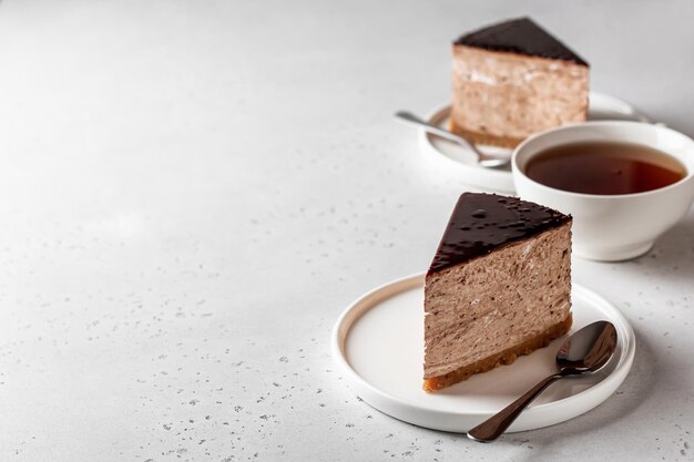 Due fette di cheesecake al cioccolato su piatti bianchi con una tazza di tè su sfondo bianco Copia spazio