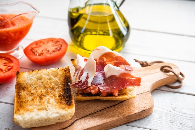 Due fette di pane tostato una con pomodoro e prosciutto iberico su tavola di legno colazione biologica