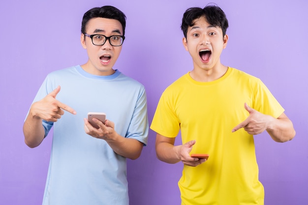 Due fratelli asiatici che usano telefoni cellulari su sfondo viola