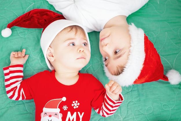Due fratelli che festeggiano il Natale indossando un cappello da Babbo Natale due bambini sdraiati su una coperta verde