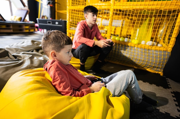 Due fratelli che giocano alla console per videogiochi seduti su pouf giallo nel centro giochi per bambini