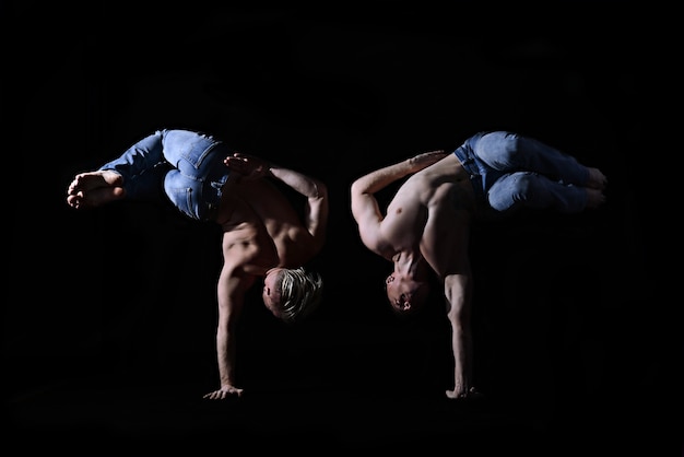 Due fratelli gemelli in blue jeans con un torso nudo eseguono elementi acrobatici, sfondo nero