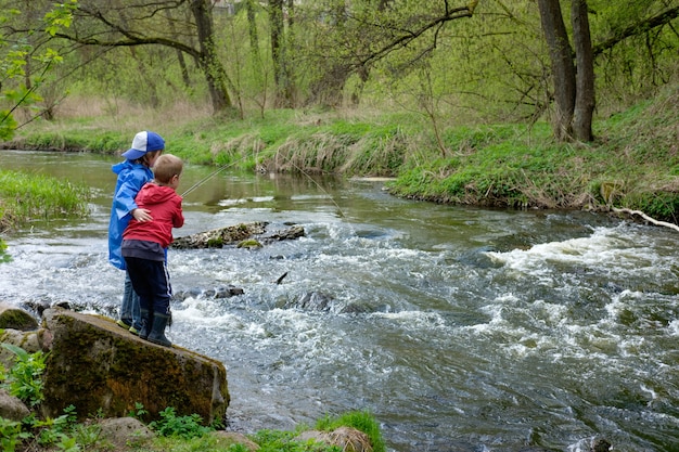 Due fratelli maschi, vestiti con un impermeabile rosso e blu, stanno pescando insieme sul fiume Mount