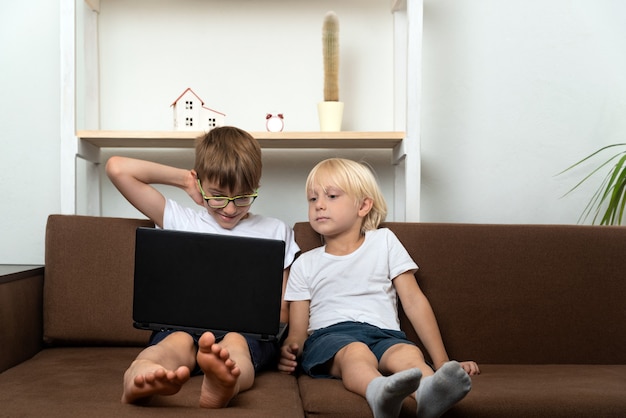 Due fratelli sono seduti sul divano e guardano laptopâ