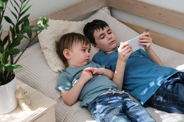 Due fratellini che guardano felici i cartoni animati insieme su uno smartphone Concetto di bambini e gadget