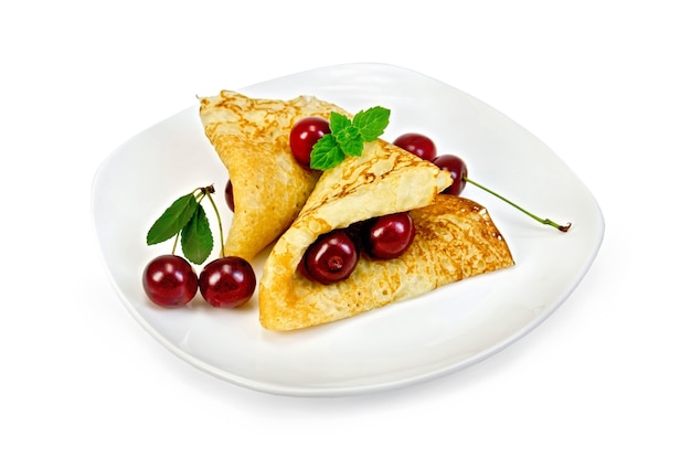 Due frittelle con ciliegie ai frutti di bosco, menta su un piatto bianco isolato su sfondo bianco