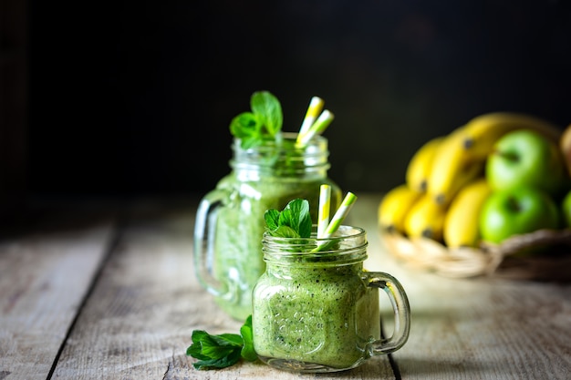 Due frullati verdi sani con spinaci, banana, mela e menta in barattolo di vetro e ingredienti. Detox, dieta, concetto di cibo sano e vegetariano. Copia spazio