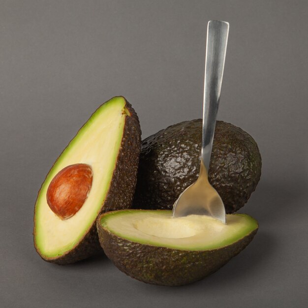 Due frutti maturi di avocado giacciono su uno sfondo grigio con un cucchiaio