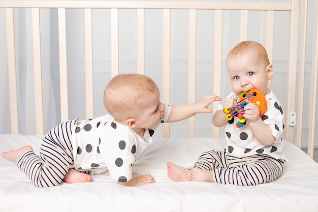 Due gemelli di 8 mesi giocano nella culla, lo sviluppo precoce dei bambini fino a un anno, il concetto di relazione dei figli di fratello e sorella, il bambino prende il giocattolo dall'altro.