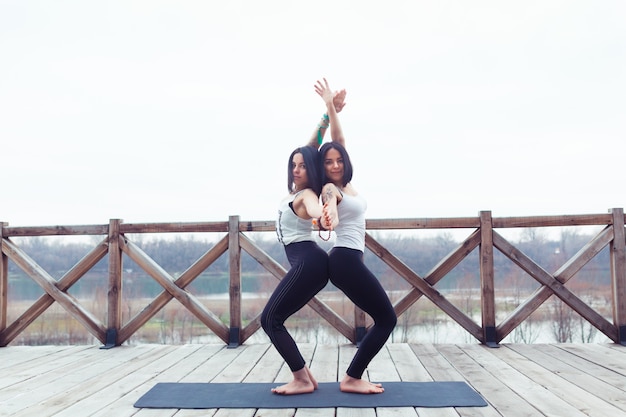 Due gemelli di donne sportive attraenti allenano la posa di yoga dell'albero su una stuoia nera all'aperto sulla natura