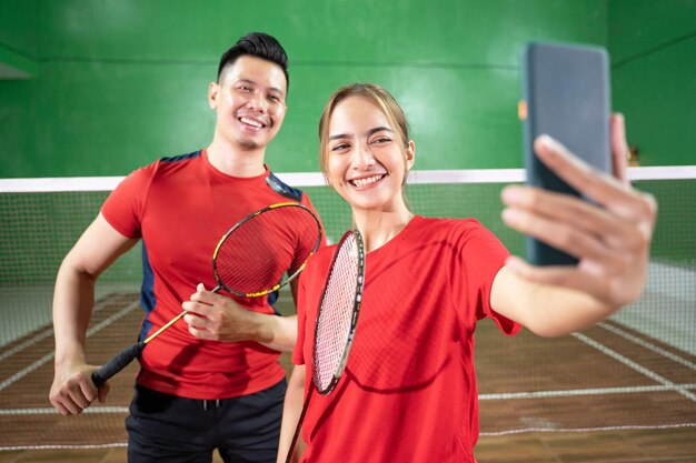 Due giocatori di badminton si fanno selfie insieme usando il cellulare mentre tengono la racchetta