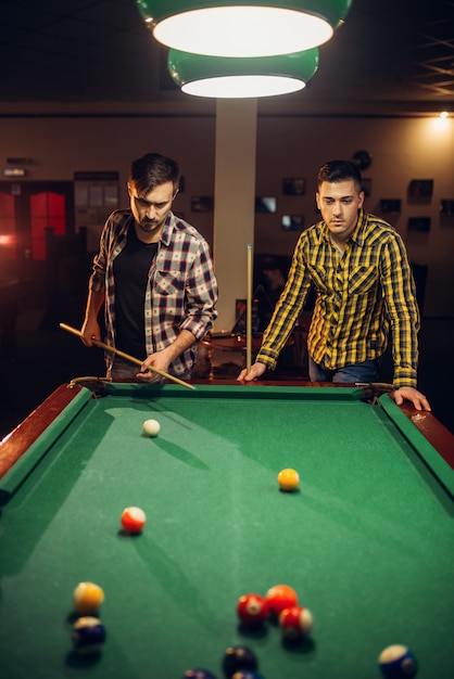 Due giocatori di biliardo maschi con stecca al tavolo con palline colorate, sala biliardo. Gli uomini giocano a biliardo americano nel bar dello sport