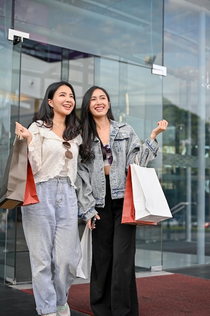 Due gioiose amiche asiatiche che escono dal centro commerciale con le loro borse della spesa