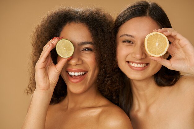 due gioiose giovani donne di razza mista che sembrano eccitate, coprendo gli occhi con limone e lime tagliati a metà