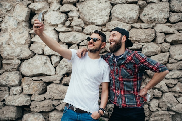 Due giovani amici eccitati che prendono un selfie sopra il fondo del muro di pietra