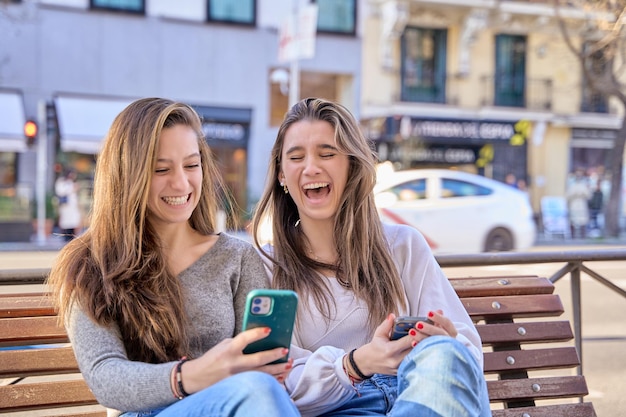 Due giovani amici si divertono guardando il telefono guardano il video online tenere il cellulare vestito con abiti casual Due amiche si divertono insieme